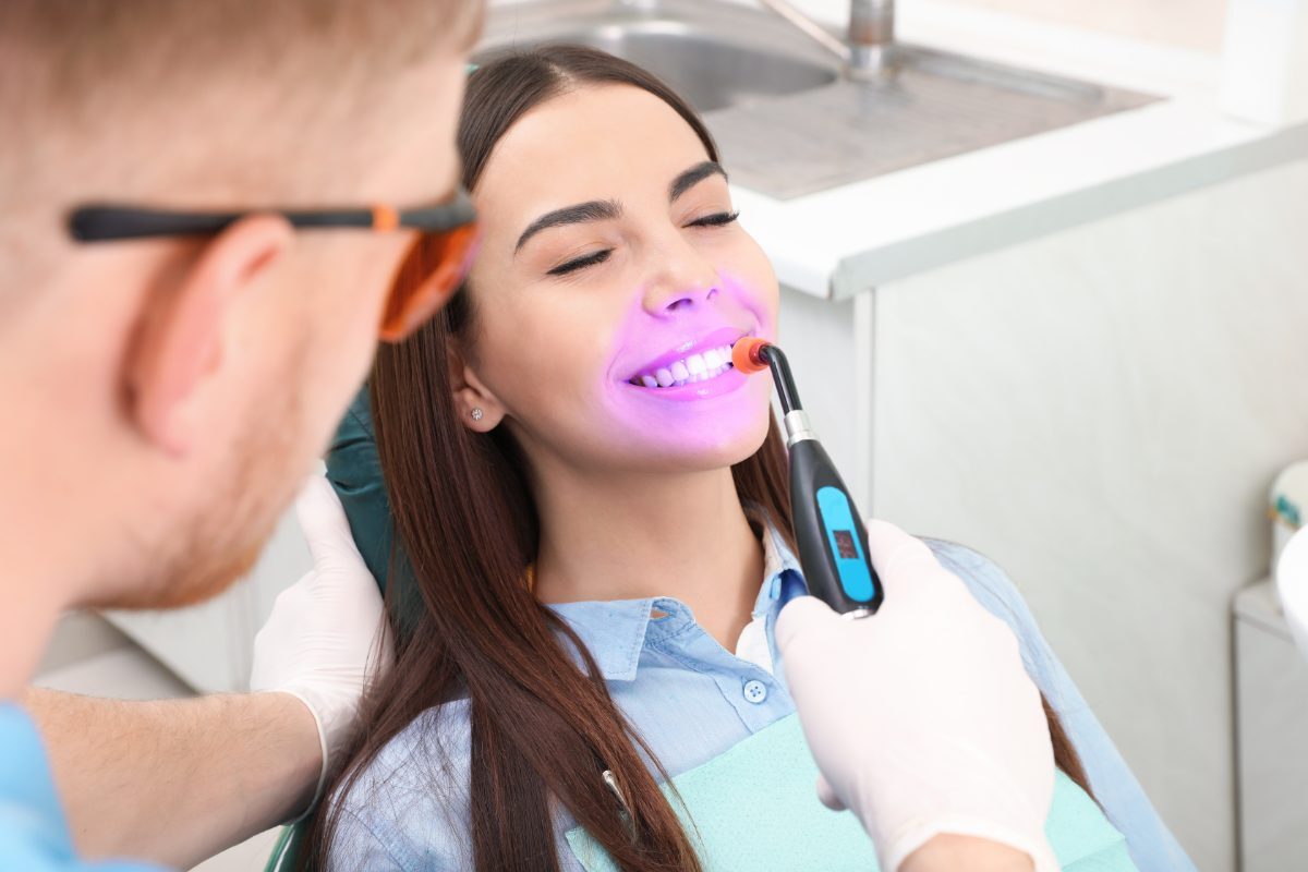 Dentist using LED whitening device on patient's teeth during cosmetic whitening treatment.